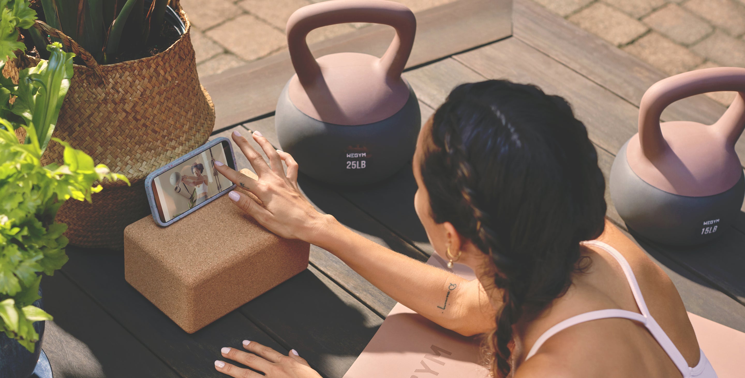 Woman using a smartphone app on a phone stand outdoors with kettlebells in the background